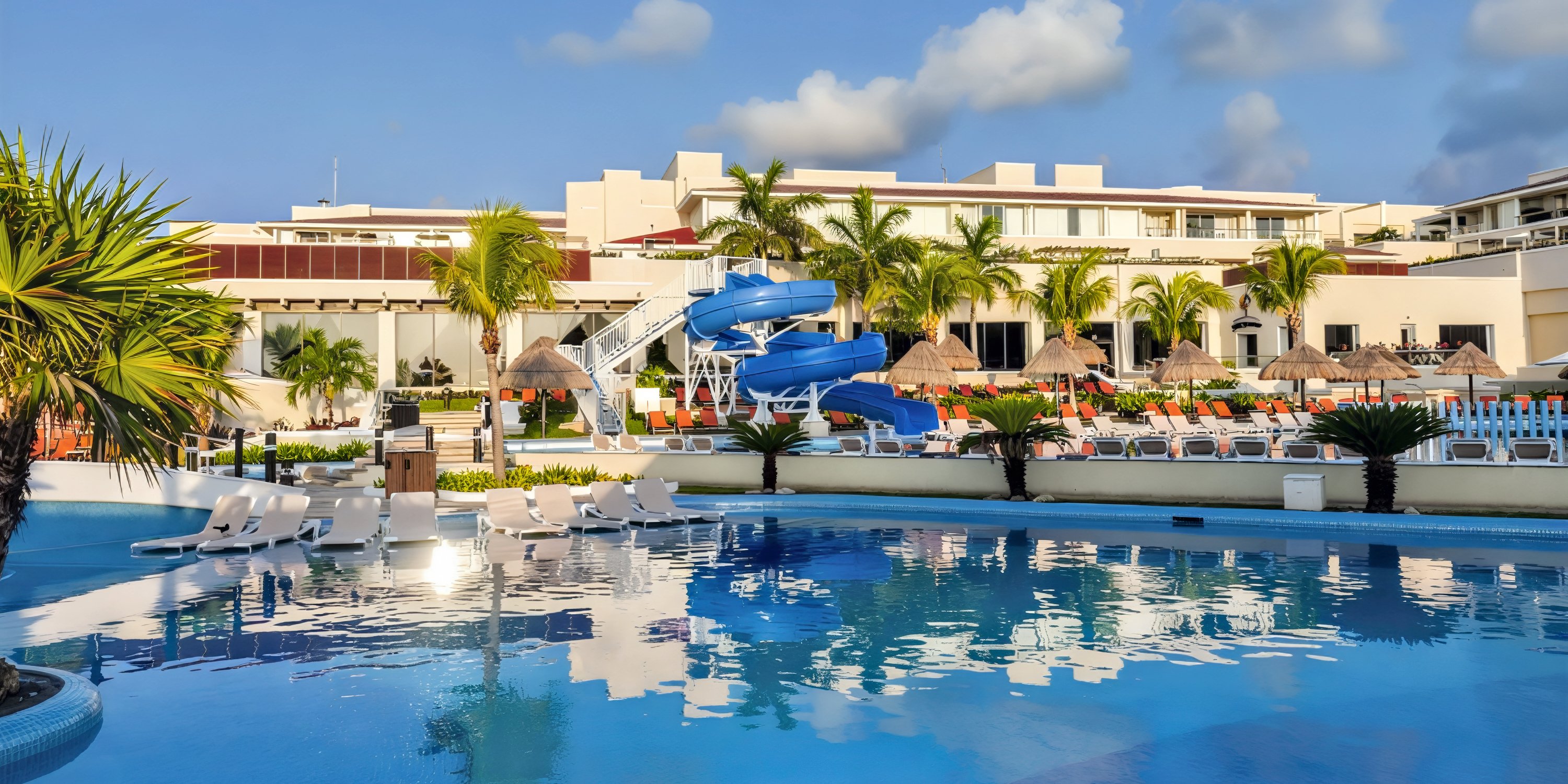 Moon Palace Nizuc: An idyllic destination wedding venue featuring an outdoor pool with lounge chairs, waterslides, swaying palm trees, and a stunning resort backdrop.