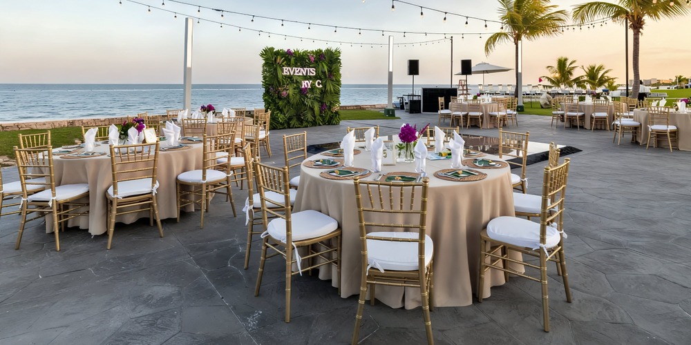 A stunning destination wedding at Moon Palace Nizuc, featuring round tables and elegant gold chairs arranged outdoors, all set against a breathtaking ocean view at sunset.