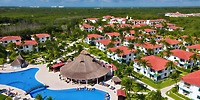 Aerial view of Ocean Coral and Turquesa, a stunning destination wedding resort featuring red-roofed buildings, swaying palm trees, and a sprawling pool.