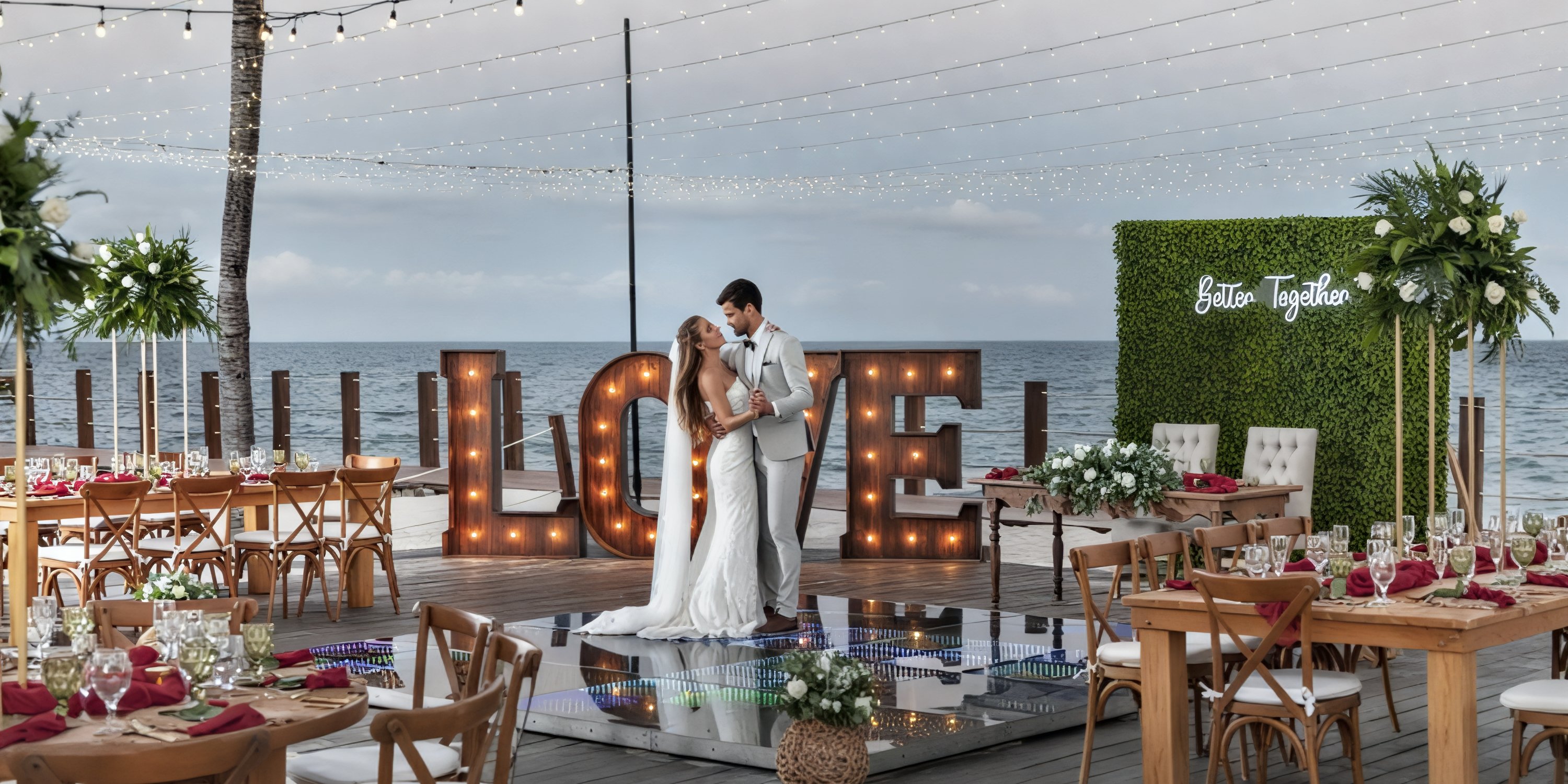 The bride and groom share an embrace on the beautifully decorated deck at Ocean Maya Royale, surrounded by glowing "LOVE" lights and a stunning ocean view—an unforgettable moment at their destination wedding.
