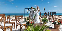The bride and groom share their first dance at a beautiful destination wedding on the beach at Ocean Coral and Turquesa, surrounded by elegant chairs and a glowing LOVE sign.