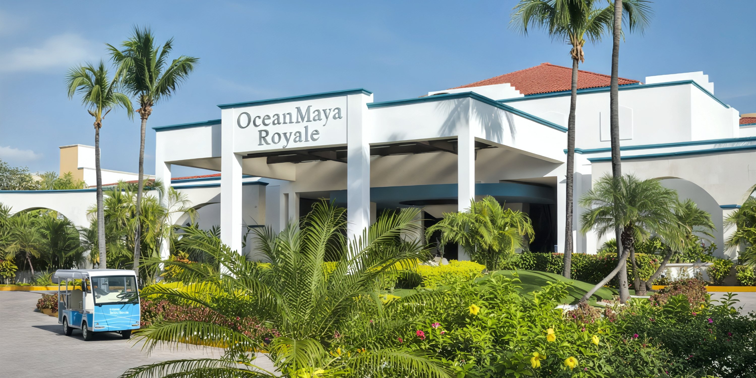 Elegant white hotel building with an “Ocean Coral and Turquesa” sign, framed by swaying palm trees and a blue shuttle at the entrance—a picturesque destination wedding venue.