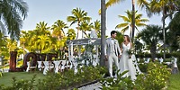 The bride and groom walk hand in hand at Ocean Maya Royale, a stunning destination wedding venue adorned with palm trees and a glowing LOVE sign.