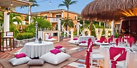 The Ocean Maya Royale is elegantly set up for a destination wedding, featuring round tables with white cushions, pink accents throughout the décor, and illuminated LOVE letters as a romantic focal point.