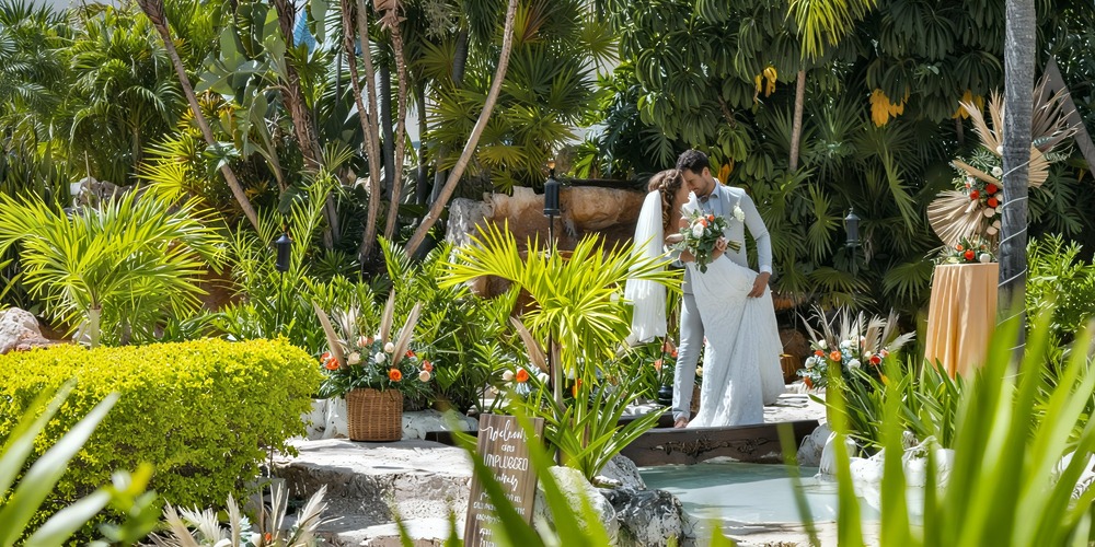 A bride and groom share a kiss during their destination wedding at Ocean Maya Royale, surrounded by the lush beauty of a tropical garden.