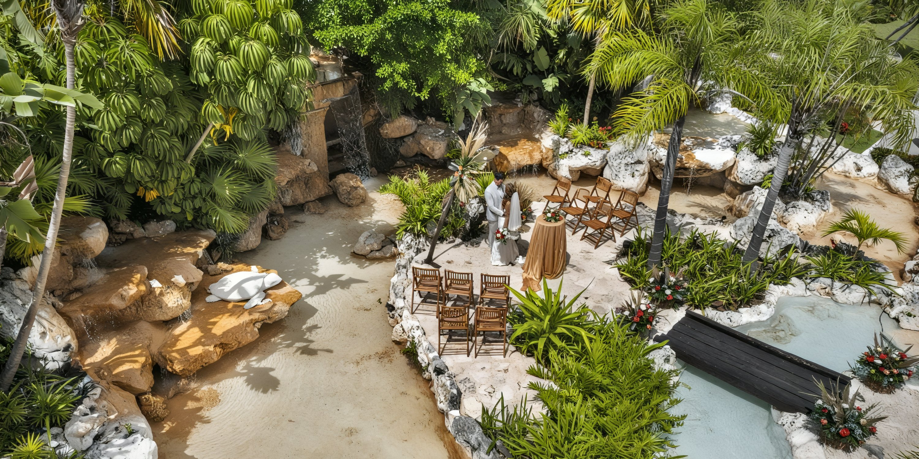 Outdoor destination wedding setup at Ocean Maya Royale, featuring elegant chairs and lush greenery adorned with beautiful flowers, all arranged beside a charming small waterfall.