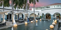 Ocean Coral and Turquesa: an idyllic destination wedding venue featuring poolside dining surrounded by swaying palm trees, elegant white awnings, and romantic sunset lighting.