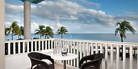 Balcony at Ocean Maya Royale featuring two chairs and a table, offering stunning views of the sandy beach and palm trees—an ideal spot for relaxing during your destination wedding.