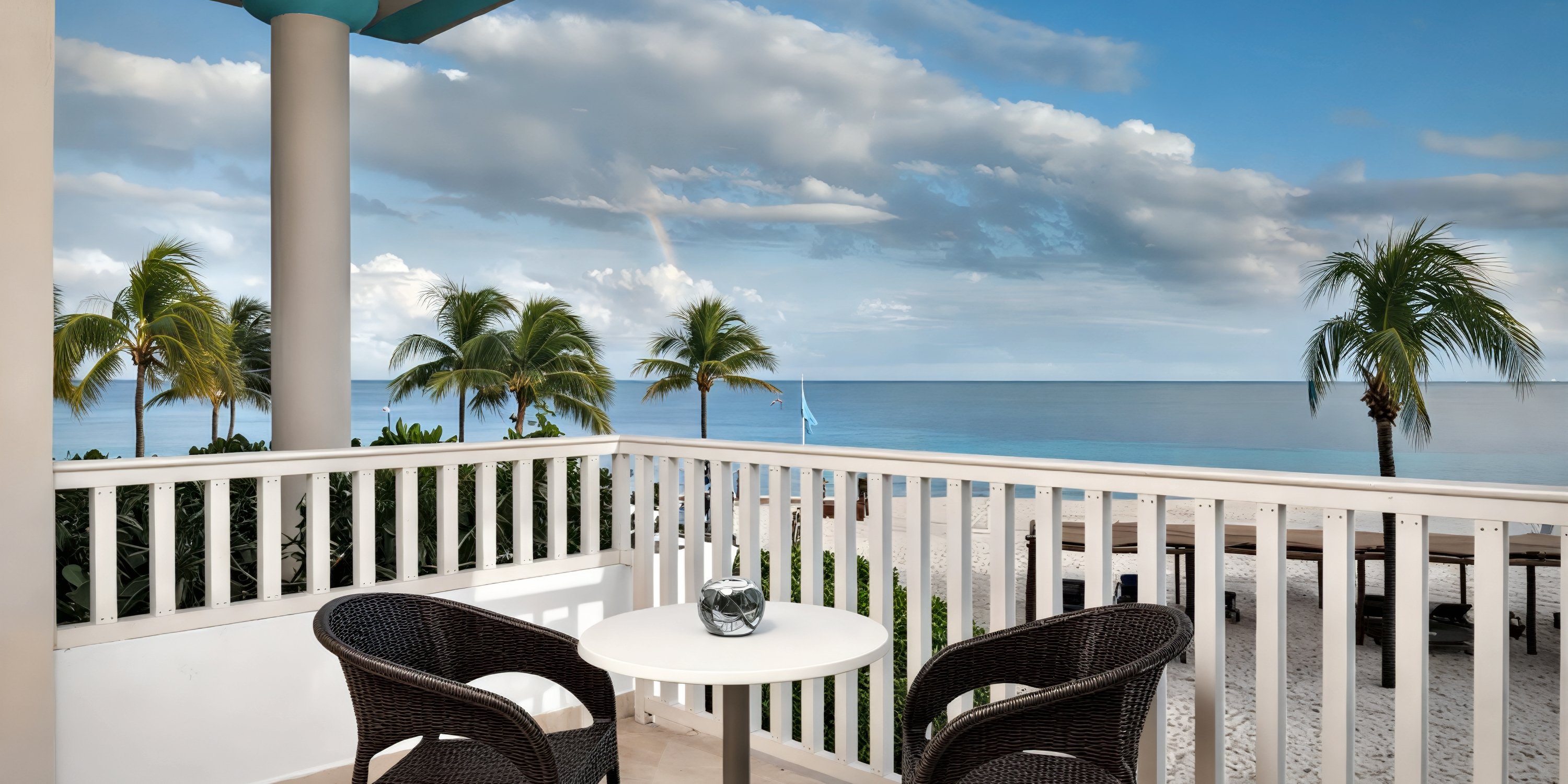 Balcony at Ocean Maya Royale featuring two chairs and a table, offering stunning views of the sandy beach and palm trees—an ideal spot for relaxing during your destination wedding.