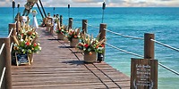 A wooden pier at Ocean Coral and Turquesa stretches out to the ocean under a partly cloudy sky, creating a perfect backdrop for a destination wedding.