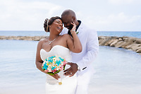 Kishan and Ericka stand by the water, smiling and embracing in their white wedding attire, capturing a perfect moment from their destination wedding.