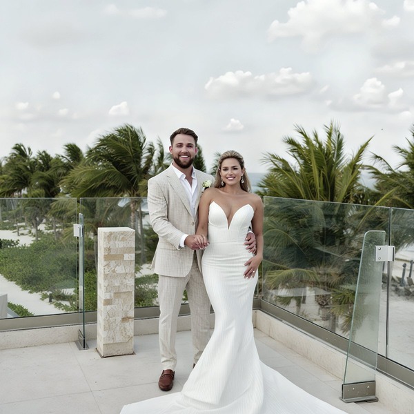 Brittiney and Franswa stand together on the terrace at their destination wedding, framed by swaying palm trees and a moody, cloud-filled sky.