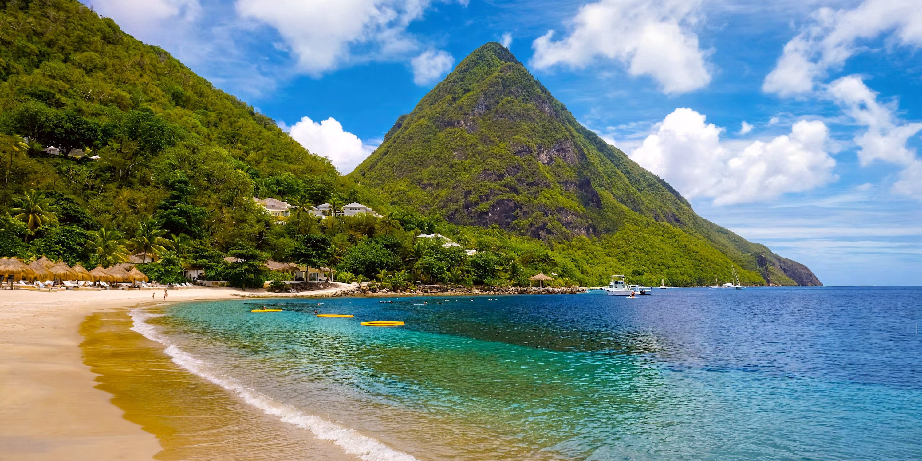 A stunning destination wedding location featuring a sandy beach with crystal-clear water, lush green hills, and a majestic mountain rising in the background.
