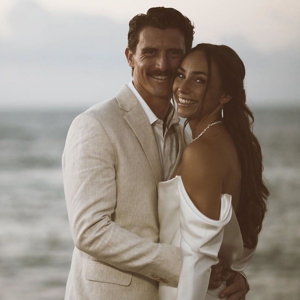 A couple dressed in formal attire shares an embrace and radiant smiles on the beach, celebrating their destination wedding.