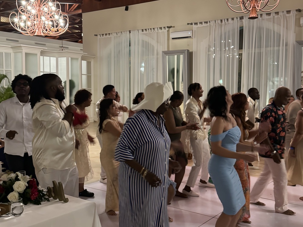 A group of people dances indoors at a destination wedding, dressed in semi-formal attire as they celebrate the special occasion.