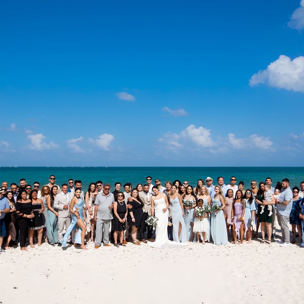 A large wedding party gathers on a beautiful sandy beach, creating the ideal setting for destination wedding packages for up to 100 guests.