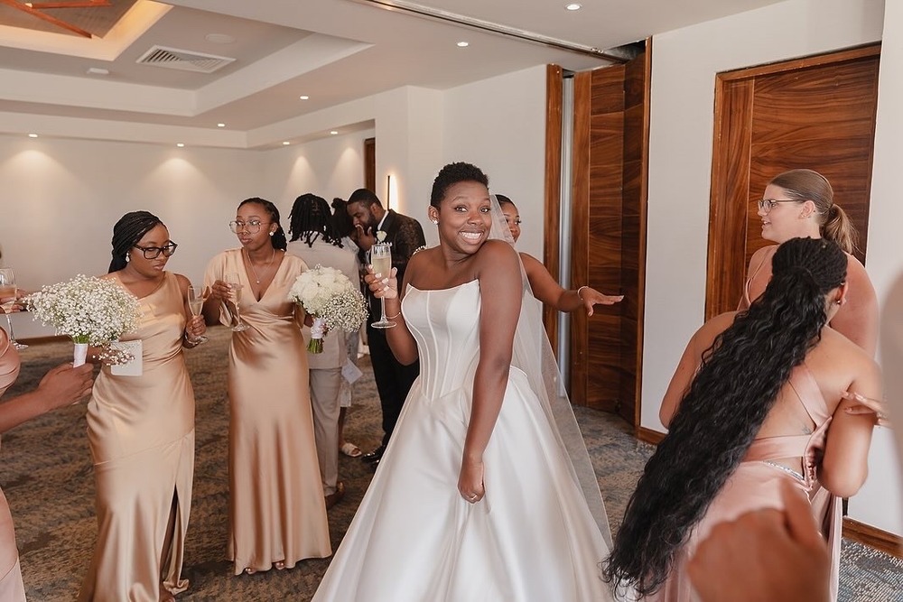 Jordan and his Kievan bride, glowing in a white wedding gown, share smiles over drinks with their bridesmaids dressed in gold inside their stunning destination wedding venue.