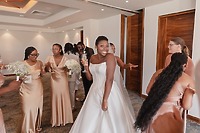 Jordan and his Kievan bride, glowing in a white wedding gown, share smiles over drinks with their bridesmaids dressed in gold inside their stunning destination wedding venue.