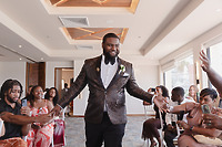 Jordan and Kievan, dressed in patterned suits, walk hand-in-hand down the aisle at their destination wedding, beaming smiles at the seated guests.