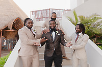 Four men pose on outdoor stairs at a destination wedding, dressed in sharp Jordan and Kievan suits—three in tan and one in a black patterned design.