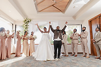 Jordan and Kievan raise their hands in celebration indoors, surrounded by their joyful wedding party at their destination wedding.