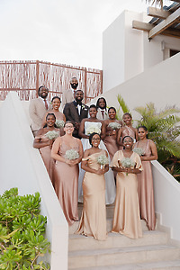Jordan and Kievan’s wedding party pose on outdoor stairs, dressed in elegant gold gowns and suits, creating a stunning scene for their destination wedding.