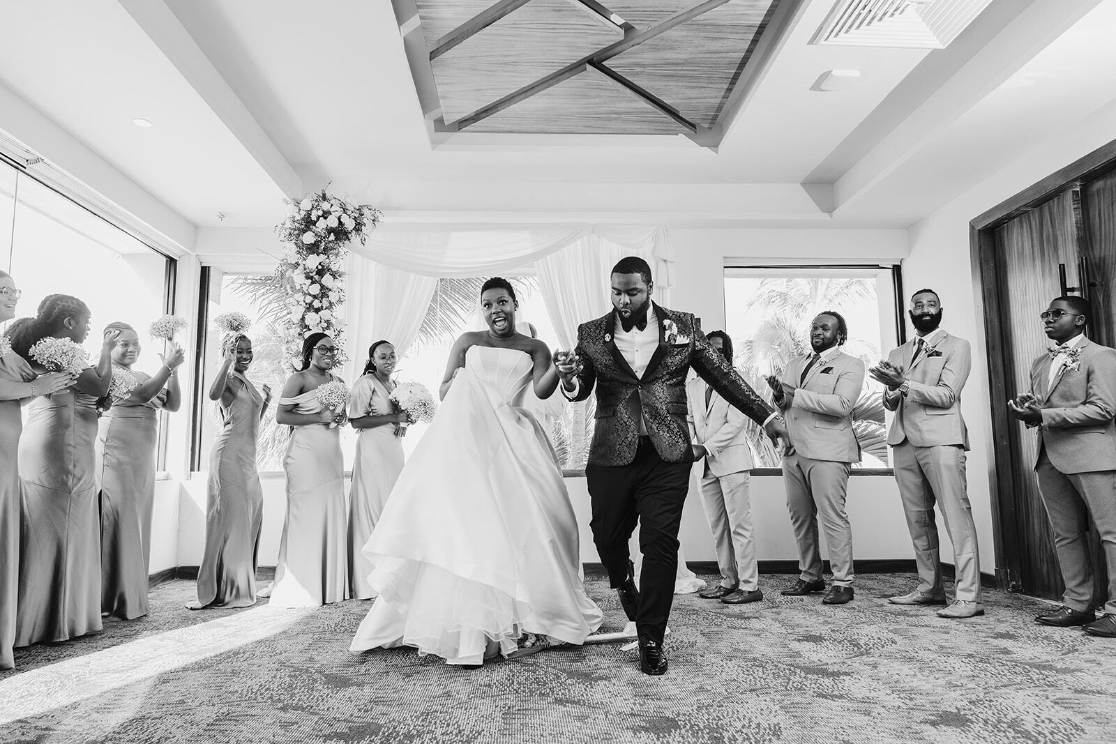 Jordan and Kievan walk down the aisle during their destination wedding, as their wedding party stands and applauds.
