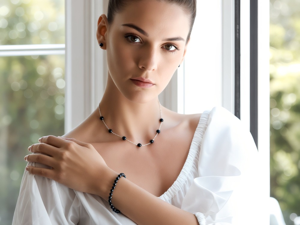 A woman in a white blouse stands by a window, wearing matching black bead jewelry—her elegant look perfect for a destination wedding.