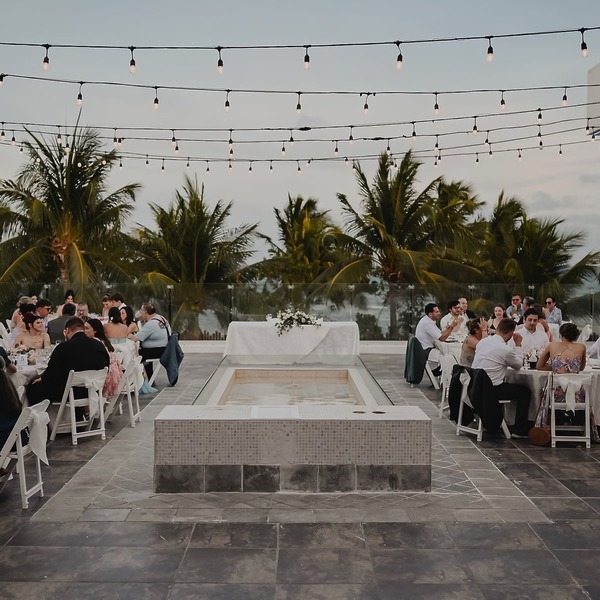 A beautiful destination wedding with guests seated at elegant tables near a sparkling fountain, twinkling string lights overhead, and majestic palm trees in the background.