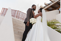Saphire and Stephen pose together on outdoor stairs during their destination wedding, with the bride holding a bouquet of white roses.
