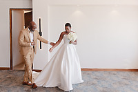 Jordan in a tan suit walks with bride Kievan in a white dress holding a bouquet at their wedding.
