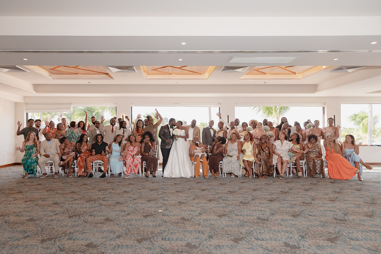Jordan and Kievan stand at the center of a large destination wedding group posing indoors.