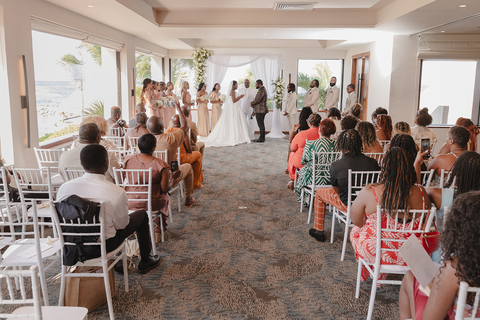 Indoor destination wedding with couple, wedding party, and guests all seated facing the altar.