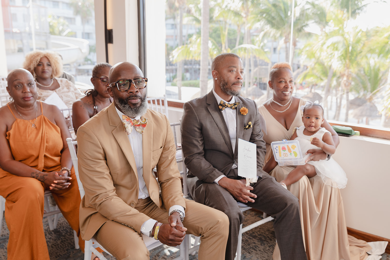 Six adults and a child in formal Jordan and Kievan attire sit by a window at a destination wedding.