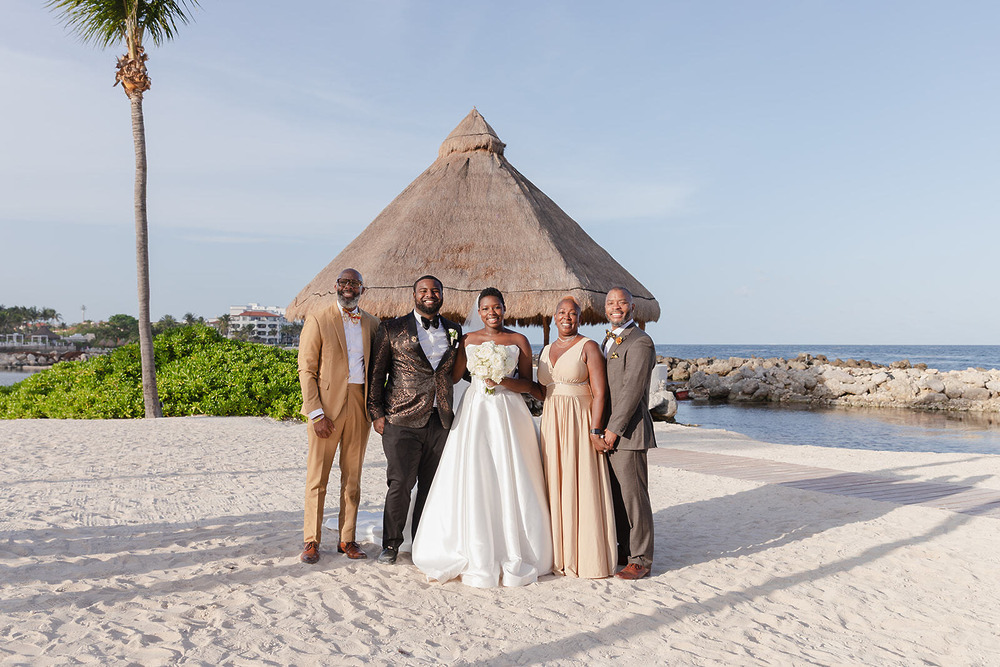 Five people pose on the beach at a destination wedding, with Saphire and Stephen in the background.