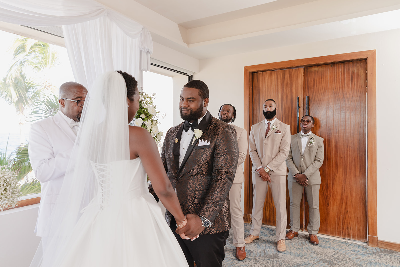 Jordan and Kievan hold hands at their beautiful indoor destination wedding as guests look on.