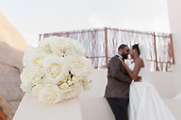 A stunning sapphire and stephanotis bouquet takes center stage, while the bride and groom share an embrace in the softly blurred background, capturing a romantic moment from their destination wedding.