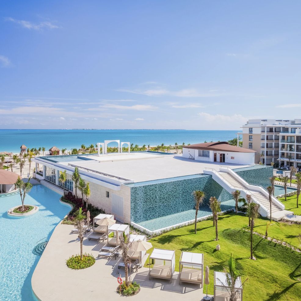 Resort pool area with cabanas, ideal for a destination wedding, overlooking ocean and modern buildings.