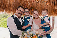 A family of four poses and smiles beneath the thatched roof at Teneal and Jonathan's destination wedding.