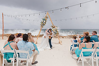 Teneal and Jonathan share a kiss at their beautiful destination wedding on the beach, surrounded by guests who watch and capture the special moment with photos.