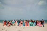 A large group gathers and cheers on a sandy beach, celebrating Sydney and Hayden's destination wedding.