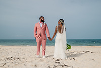 Sydney and Hayden holding hands on a sandy beach with the ocean in the background, capturing a perfect moment from their destination wedding.