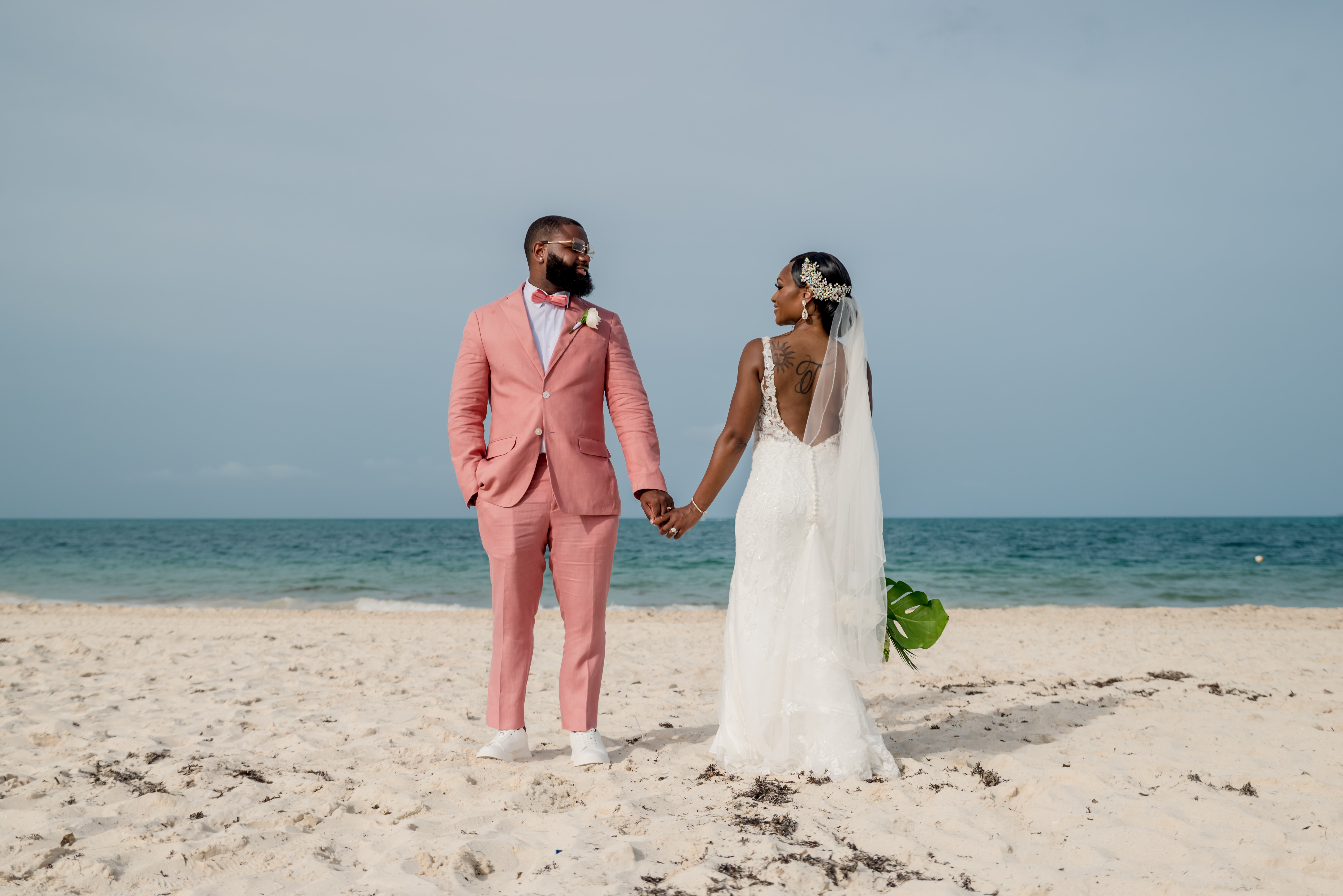 Sydney and Hayden holding hands on a sandy beach with the ocean in the background, capturing a perfect moment from their destination wedding.