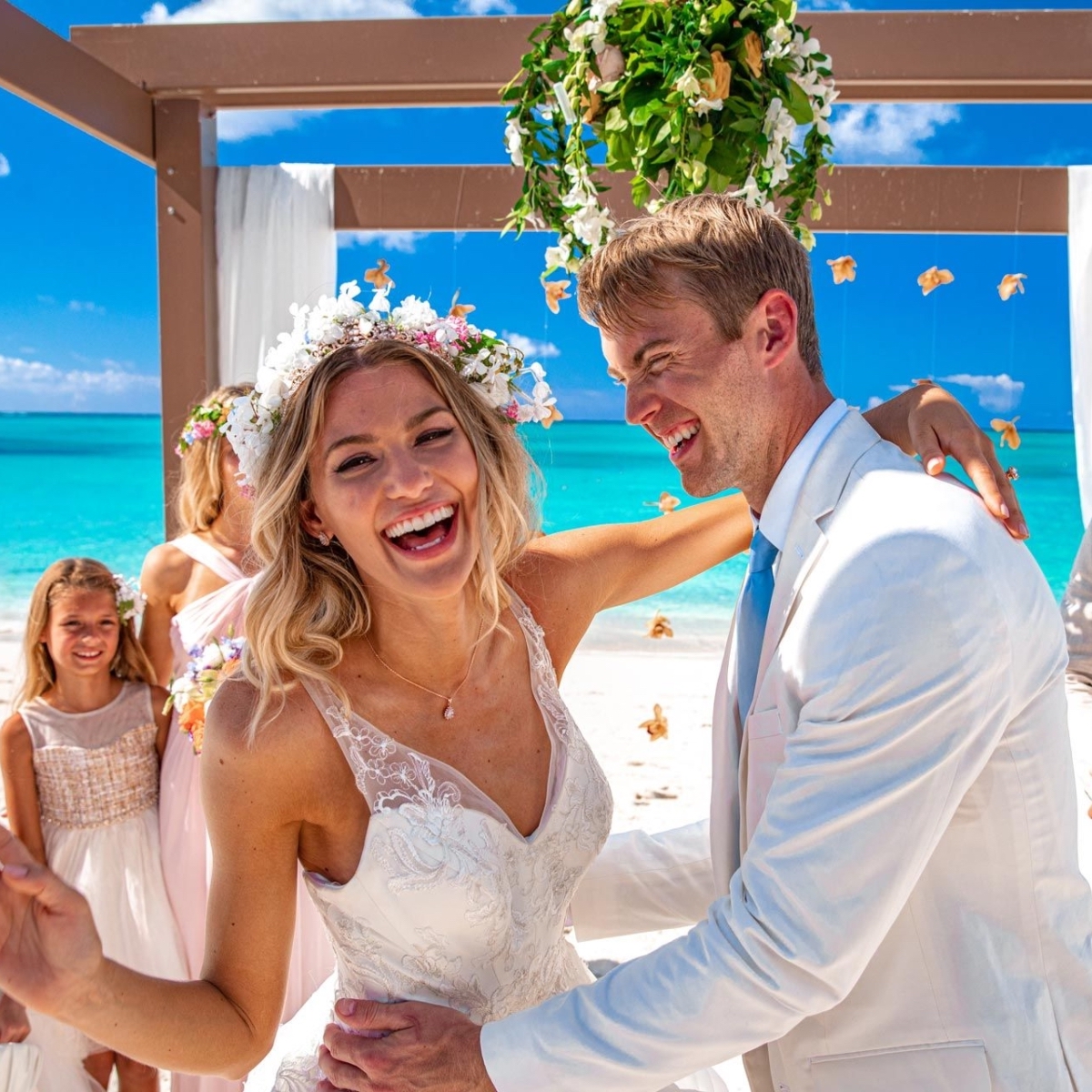 The smiling bride and groom share a joyful dance at their destination wedding, with the turquoise ocean creating a stunning beachside backdrop.