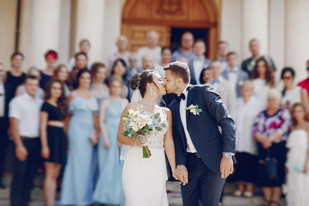 The bride and groom share a kiss on the outdoor steps, surrounded by their wedding guests at the destination wedding.