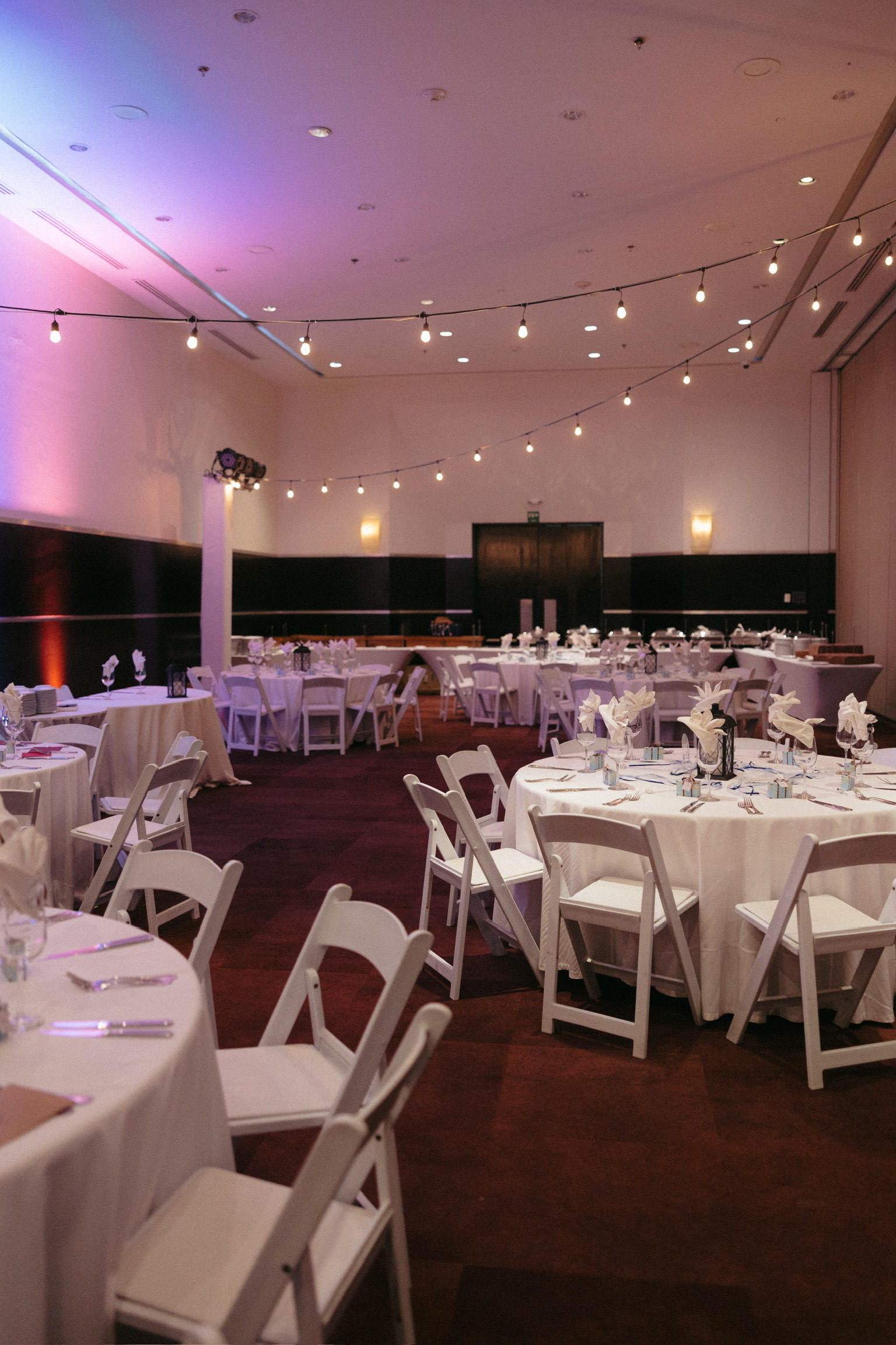 Stephanie and Mark's destination wedding: round tables fill a banquet hall with overhead string lights.