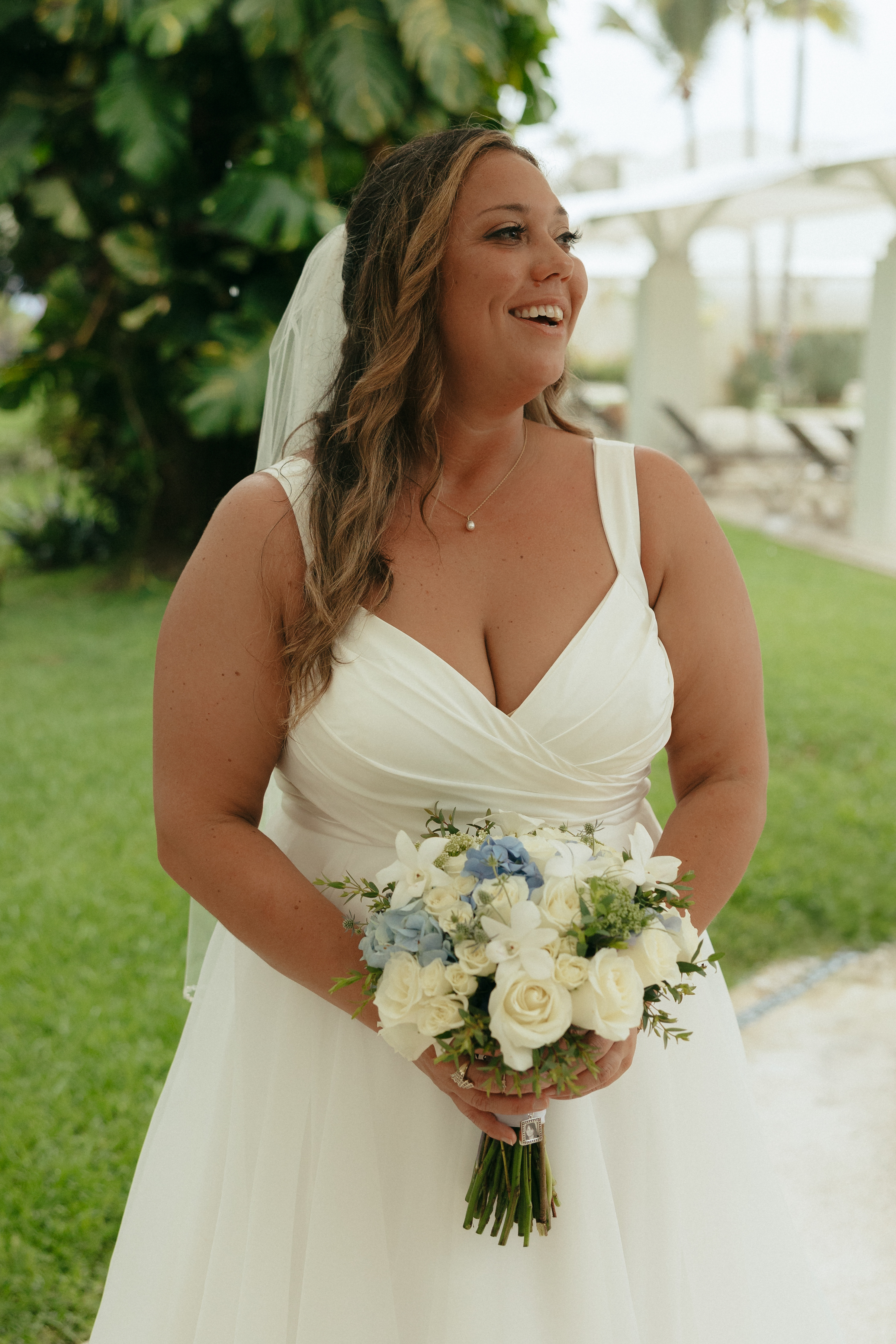 Bride in a white wedding dress holding a blue and white bouquet, smiling happily at her wedding.