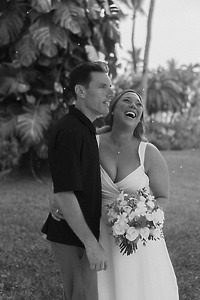 Stephanie and Mark stand outdoors at their destination wedding as Stephanie laughs, holding her bouquet.