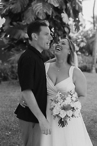 Stephanie and Mark smile outside at their wedding, she in a white dress holding her bouquet.