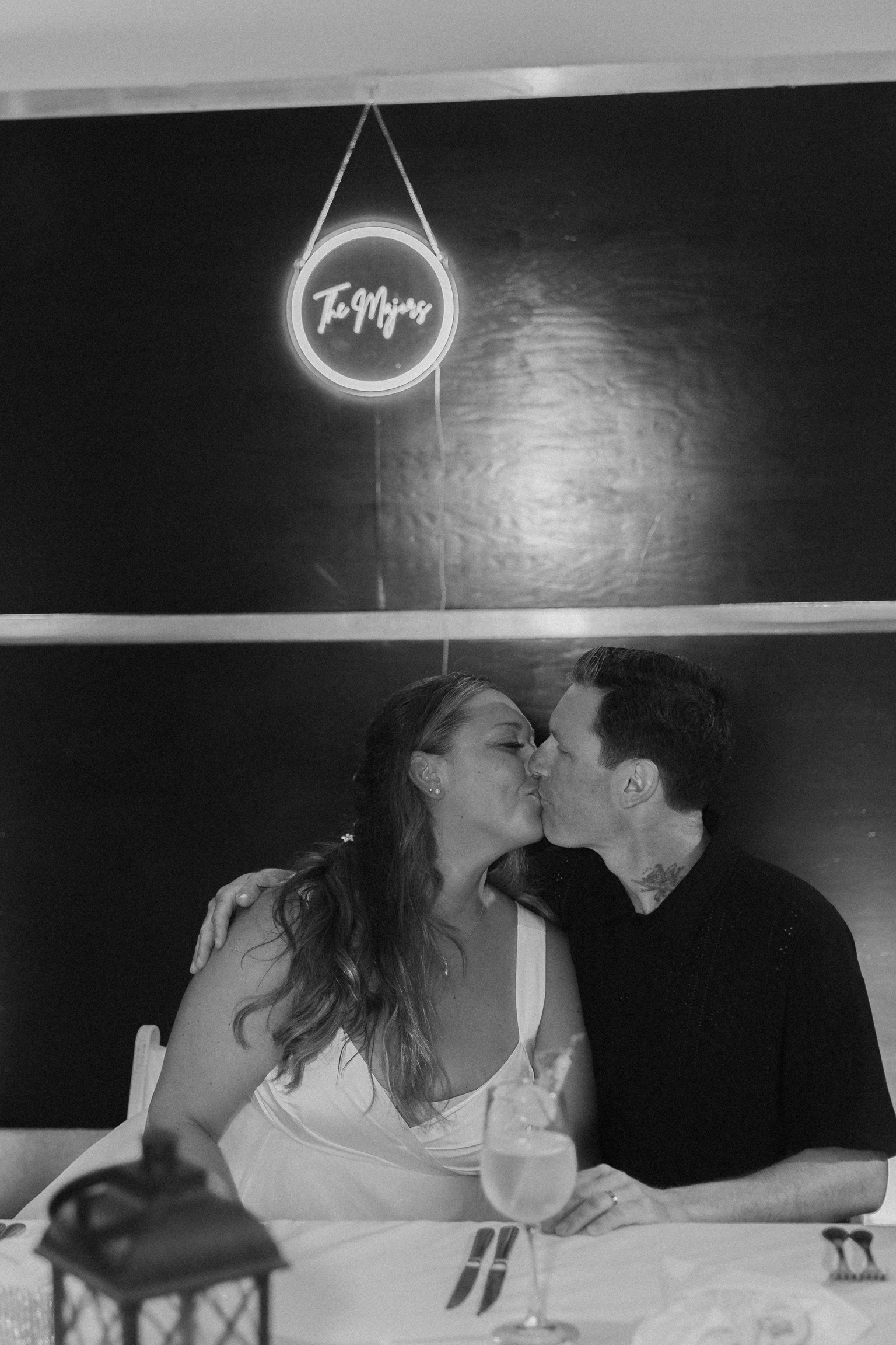 A couple kisses at their destination wedding dinner beneath a neon sign that reads "Stephanie and Mark.